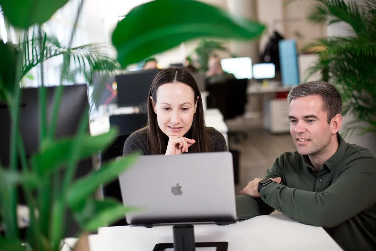 Zwei Kollegen arbeiten gemeinsam am Onboarding am Laptop in einem modernen Büro